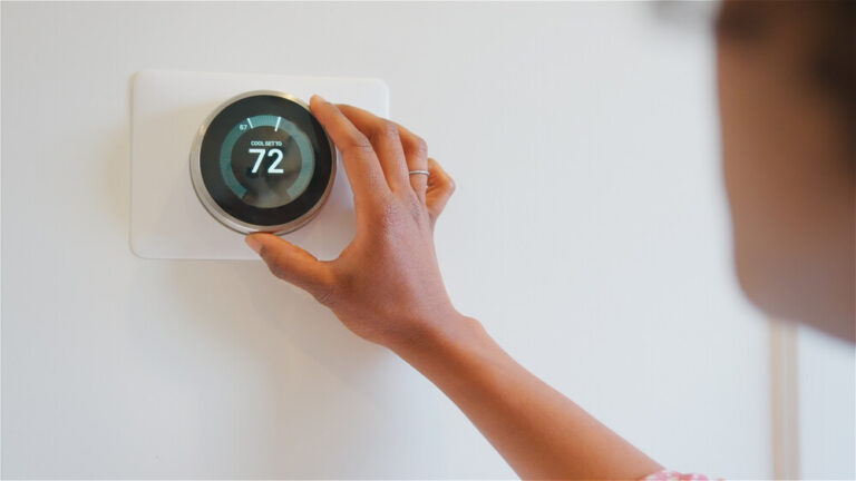 A person adjusting a smart thermostat, one of the eco friendly home improvements you can do to your Hawaii vacation rental.
